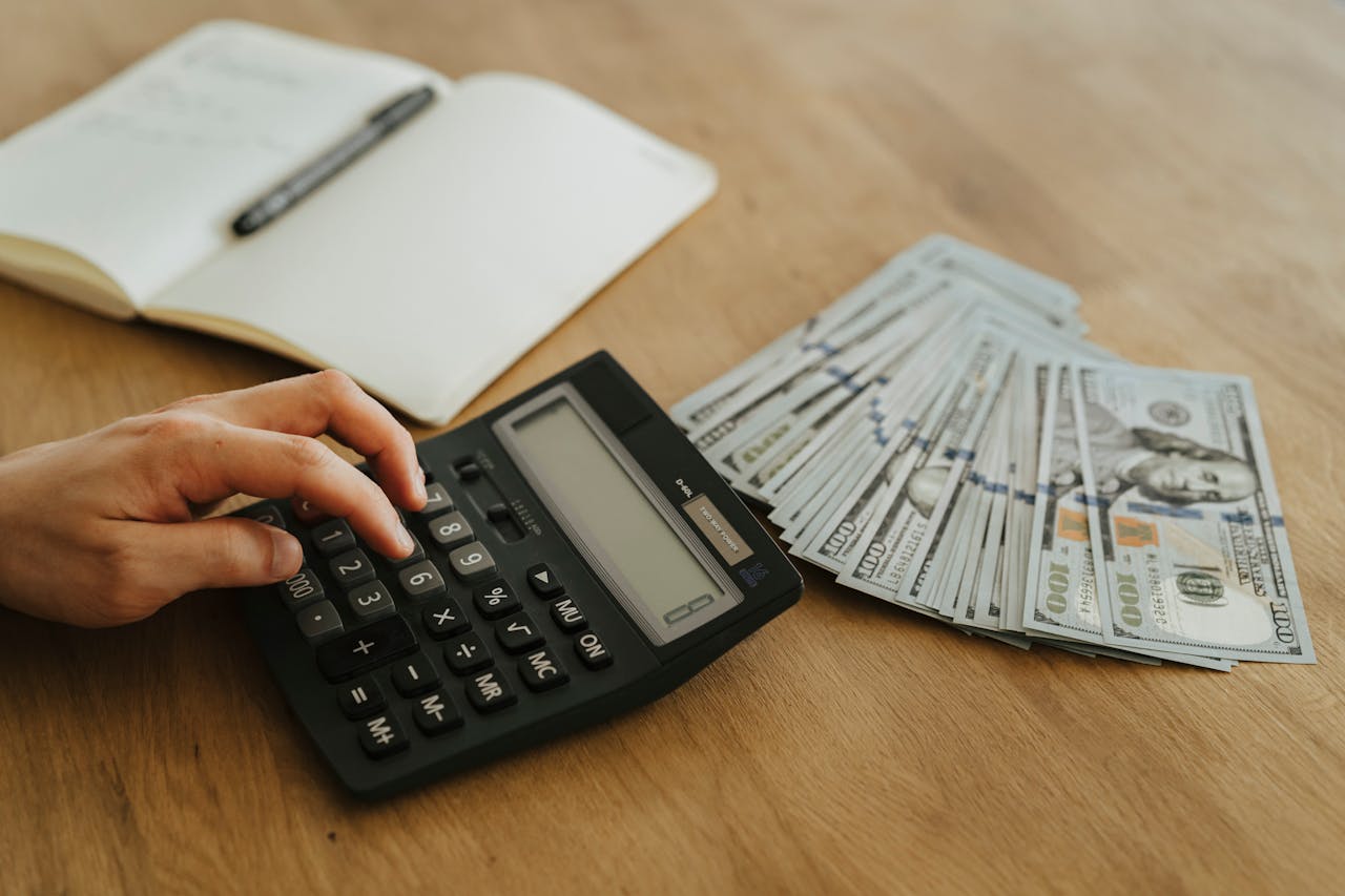 Mastering the First Impression: Your intriguing post title goes here Close-up of a hand using a calculator with cash and a notebook on a wooden table.